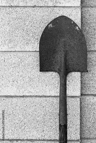 Old rusty shovel against a block wall. Black and white image.