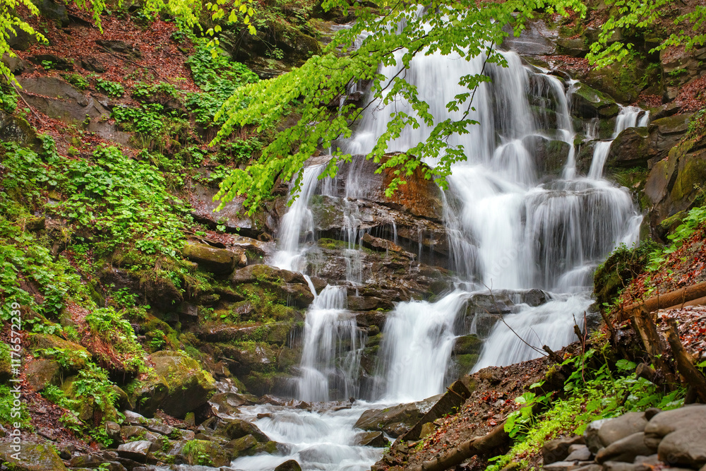 Majestic waterfall cascades through lush forest during a serene summer afternoon