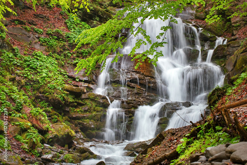 Obraz na płótnie Majestic waterfall cascades through lush forest during a serene summer afternoon w salonie