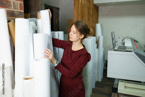 Woman removing roll of paper and standing near printer at printing studio photo