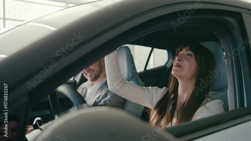 Side camera view of positive woman exclaiming with joy while sitting at driver seat in new car. Husband smiling while sitting besides her. Shopping for new vehicle. Positive emotions.