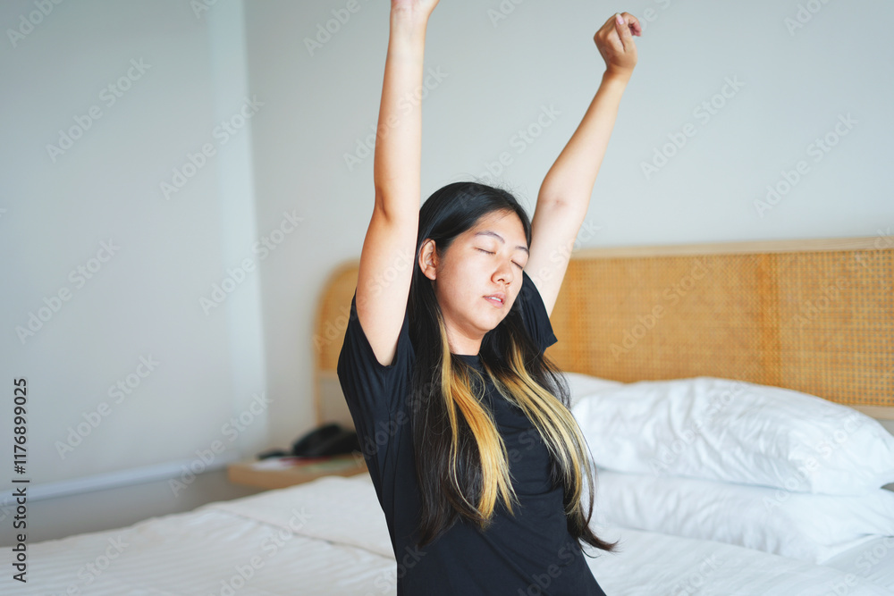 Young asian woman smiling and sitting on bed at home after waking up from good sleep in weekend and stretching her hands and body in fresh early morning, relax peaceful morning routine yawn concept. Young asian woman smiling and sitting on bed at home after waking up from good sleep in weekend and stretching her hands and body in fresh early morning, relax peaceful morning routine yawn concept.