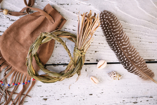 Sweetgrass braid (Hierochloe odorata), also called vanilla grass, on a medicinal pouch and smudging feather on old white wood. Overhead view.