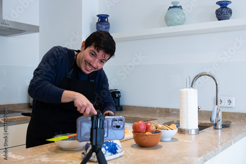 Cheerful young man cutting with a knife some apples making a tutorial of a recipe of a dessert with apples and cookies at home photo