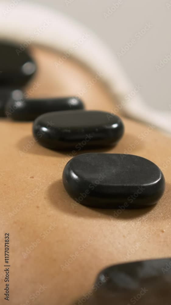 Masseuse placing hot stones on client's back. Vertical Masseuse placing hot stones on client's back. Vertical