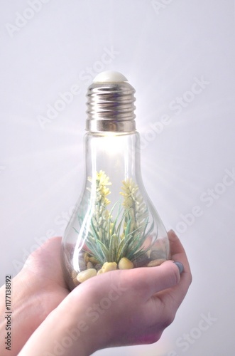 hand holding a bulb with light and green plant inside