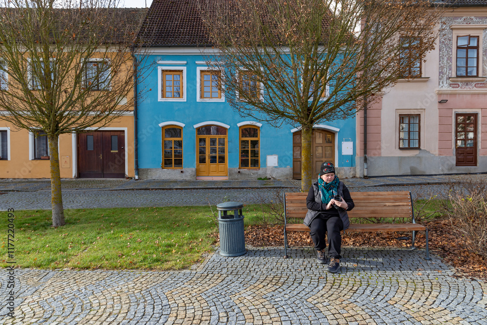 A woman with a camera sitting on a bench in an autumn city.