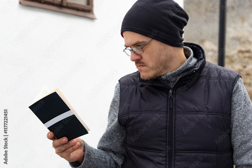 A man reading a book outdoors in an autumn city.
