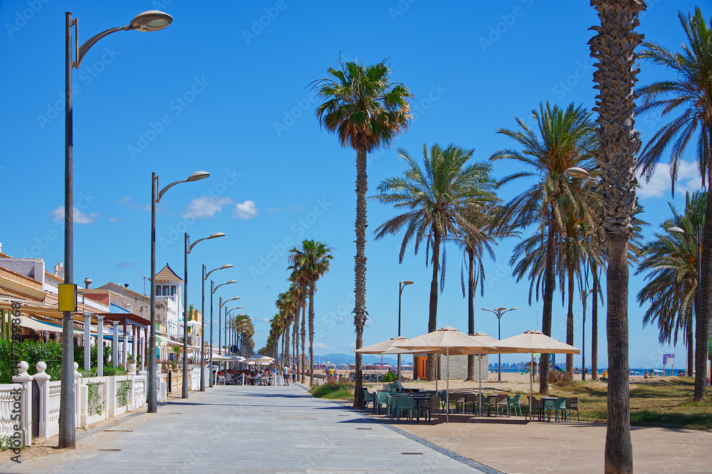 Obraz premium View of a vacations area at the seaside with coffeeshops, palm trees, blue sky and sea
