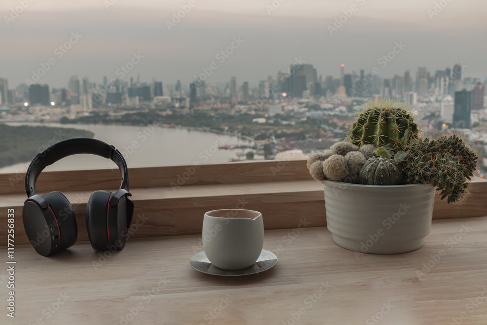 Relaxation area or Working space in Condominium balcony overlooking river view. Ear headphones, Tea cup and Cactus pot on Wooden table, use it as your Wallpaper, Poster and Copy space, Selective focus