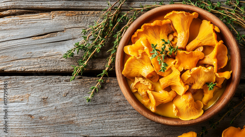 Yellow chanterelles in a wooden bowl, garnished with fresh thyme sprigs, on an aged wooden table background