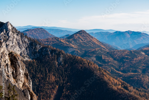 Scenic view of hilly landscape and mountains of Graz Highland and Glein Alps shrouded in mist seen from Pribitz, Hochschwab Alps, Styria, Austria. Rolling hills covered in forest vibrant autumn colors photo