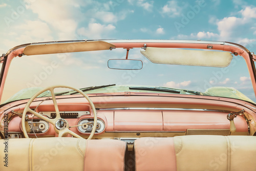 Driver view of a pink vintage classic open American cabriolet car in front of a sunny blue sky
