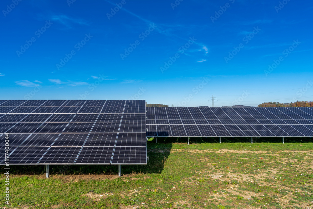 Photovoltaikanlage auf grüner Wiese mit Stromtrasse im Hintergrund Photovoltaikanlage auf grüner Wiese mit Stromtrasse im Hintergrund