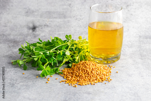 fresh fenugreek leaves, fenugreek seeds, and a glass of golden soaked fenugreek water on a grey background. photo