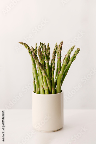 Several green asparagus in a large beige cup.