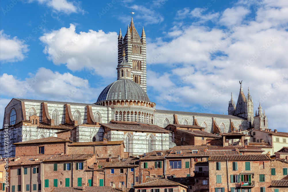 Siena's stunning cathedral towers above the medivial buildings under a blue sky with fluffy clouds