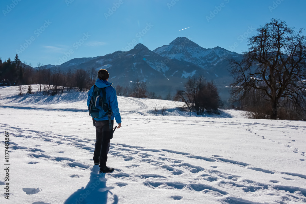 Active man on snow covered alpine meadow with panoramic view of majestic snow-capped mountain peaks Karawanks in Carinthia, Austria. Snow shoeing in winter wonderland near Villach, Austrian Alps