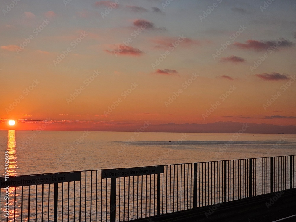 Obraz premium Genova, Italy - December 29, 2024: Background of beautiful sunset over Mediterranean sea waves. Selective focus. Beautiful red and orange sunrise over the sea. Beautiful seascape scenery, Amazing ligh
