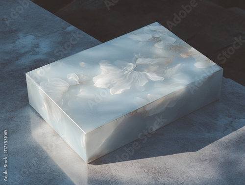 The image shows a large, reflective metallic cube placed on a white surface, with a cityscape and a cloudy sky in the background. The cube's shiny surface reflects the surrounding environment photo