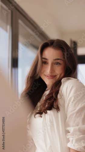 A smiling young woman looking at her reflection in a mirror, preparing and adjusting her appearance thoughtfully before attending a meeting.