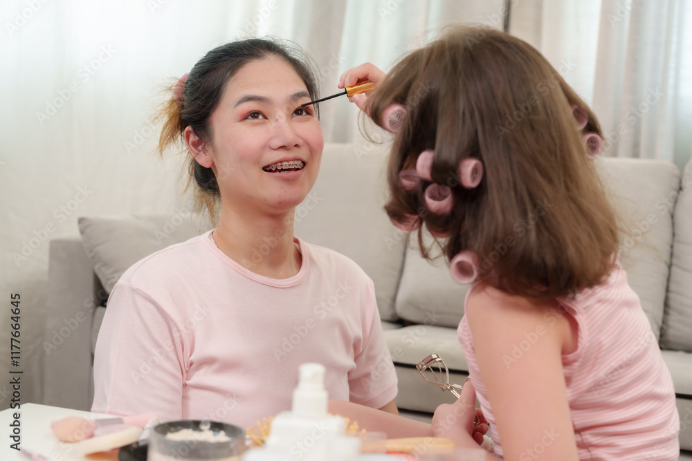 Asian mother smiling warmly as her daughter applies mascara during fun makeup session. A joyful bonding activity portraying love, laughter, and creativity in a relaxed and happy home setting. Asian mother smiling warmly as her daughter applies mascara during fun makeup session. A joyful bonding activity portraying love, laughter, and creativity in a relaxed and happy home setting.