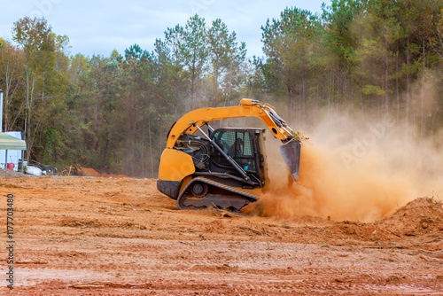 Construction vehicle prepares plot of land by moving dirt amid dust trees for future development activities