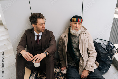 High-angle view of empathic businessman in suit talking with homeless man, showing empathy for social issues. Concept of human connection and listening to address homelessness and poverty in cities. photo