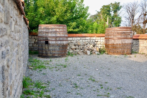 Stone walls of an ancient fortress with two large wooden barrels in the foreground. Green trees in the background. Atmosphere of history, architecture and nature.