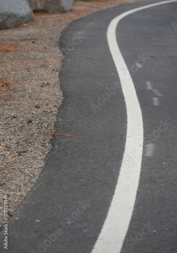 Looking down at white line road shoulder with dirt and boulders on edge of road in parking lot. photo