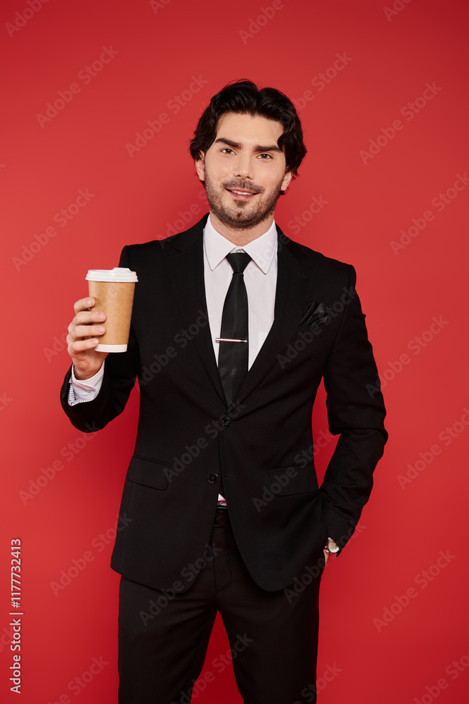Handsome young man in formal attire holding coffee against a vibrant red backdrop Handsome young man in formal attire holding coffee against a vibrant red backdrop