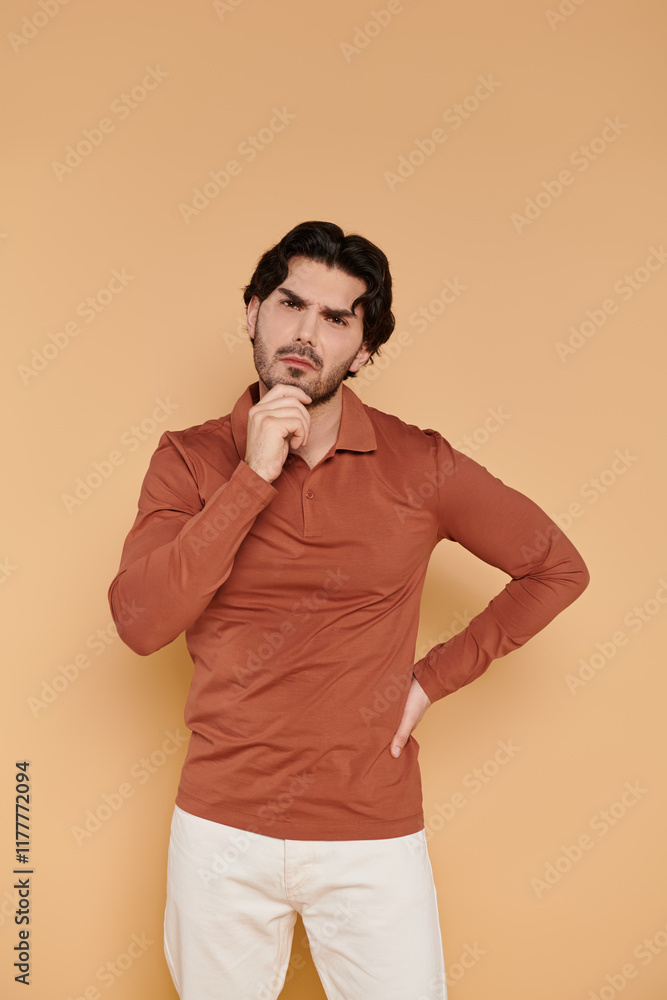 Handsome young man posing thoughtfully against a warm, minimalist backdrop Handsome young man posing thoughtfully against a warm, minimalist backdrop