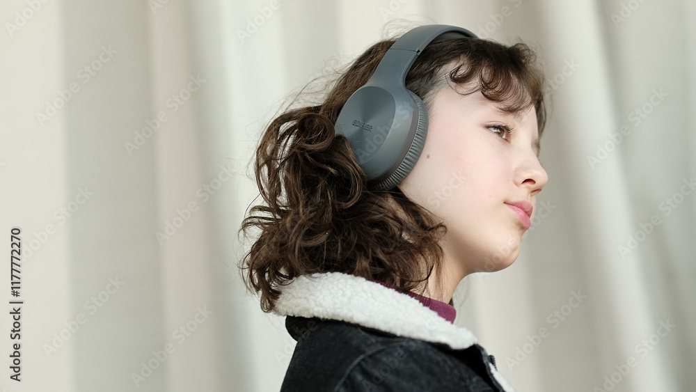 A girl wearing headphones maintains a calm, confident demeanor, immersed in her environment. This photo portrays individuality, focus, and relaxation through music. A girl wearing headphones maintains a calm, confident demeanor, immersed in her environment. This photo portrays individuality, focus, and relaxation through music.