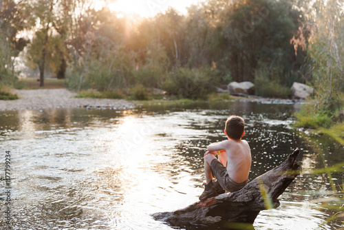 Young boy sits on a stump at the rivers edge photo