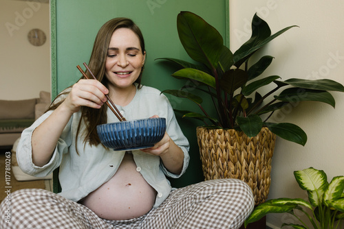 A pregnant woman sitting on the floor with a bowl and chopsticks photo