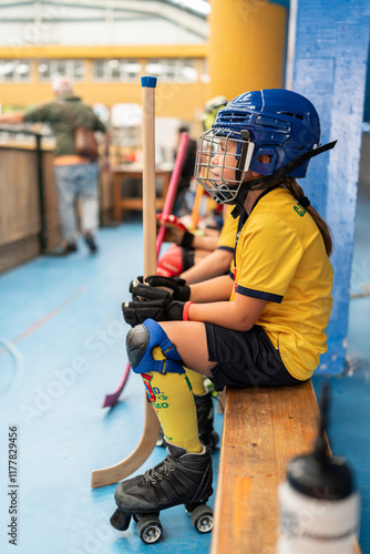 Young roller hockey player sitting on bench holding stick