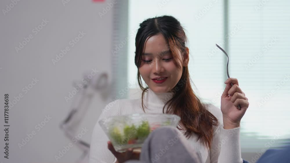 Young asian woman enjoying fresh, colorful salad while sitting comfortably on living room sofa, embodying healthy lifestyle and wellness Young asian woman enjoying fresh, colorful salad while sitting comfortably on living room sofa, embodying healthy lifestyle and wellness