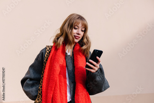 A young woman checks her smartphone while wearing autumn outfit photo