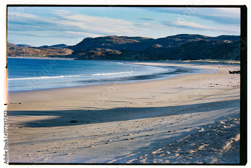 Serene beach landscape at sunset with gentle waves and mountains. photo