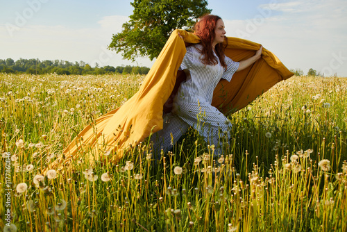 A woman with a blanket runs through a field of dandelions. photo