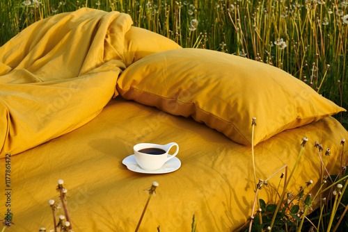 A cozy bedding setup in a dandelion-filled meadow with coffee photo