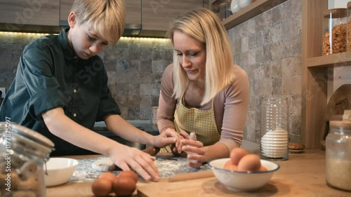 A mother and her son are in the kitchen preparing dough together for baking cakes, working side by side and enjoying the process.