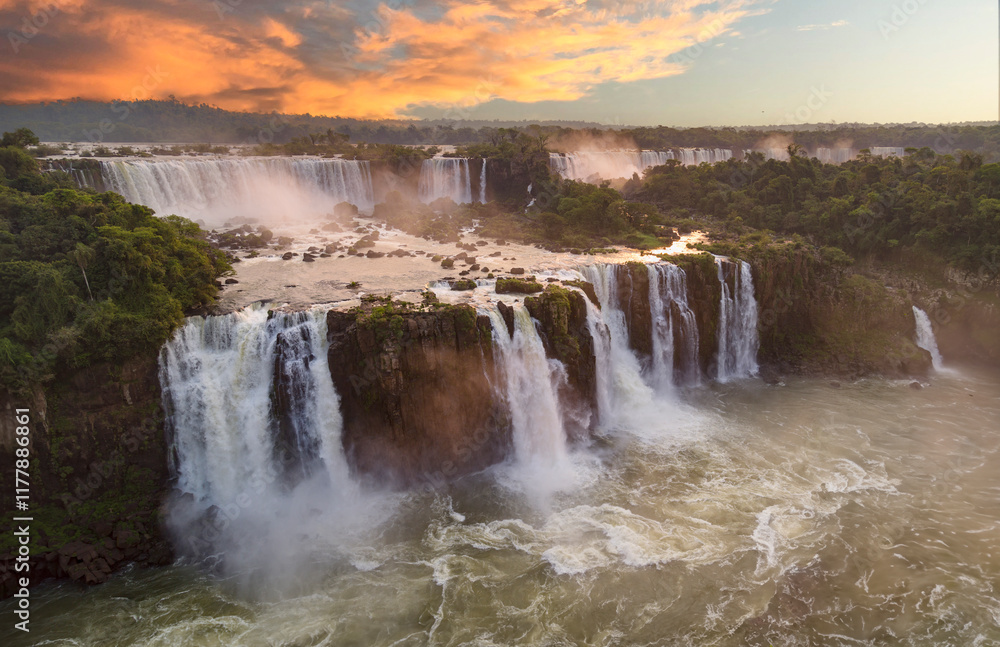 Majestic Iguazu Falls with powerful cascades flowing amidst lush green vegetation, illuminated by a vibrant sunset sky