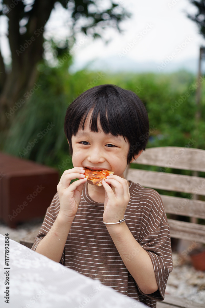 Chinese boy happily eats his homemade pizza in the backyard