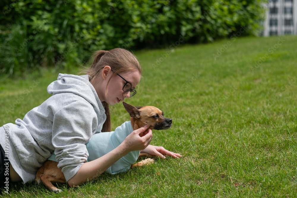 Young Caucasian woman lying on the lawn while walking with a small dog. Young Caucasian woman lying on the lawn while walking with a small dog.