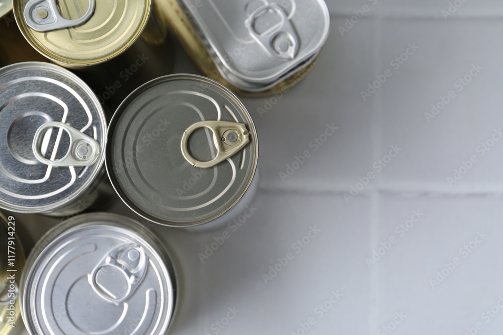 Many closed tin cans on white tiled table, flat lay. Space for text Many closed tin cans on white tiled table, flat lay. Space for text