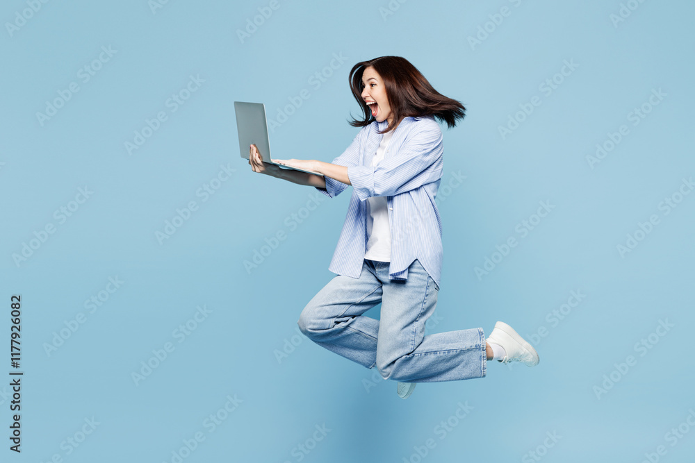 Full body young Caucasian IT woman she wears shirt casual clothes jump high hold use work on laptop pc computer isolated on plain pastel light blue cyan background studio portrait. Lifestyle concept. Full body young Caucasian IT woman she wears shirt casual clothes jump high hold use work on laptop pc computer isolated on plain pastel light blue cyan background studio portrait. Lifestyle concept.