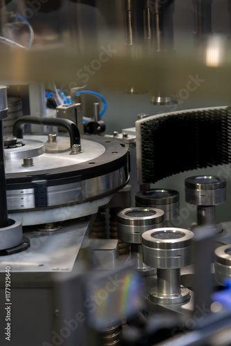 Close-up view of working modern empty metal bottle label applying machine on bottling plant. Soft focus. Copy space. Industrial food and drink technology equipment theme.