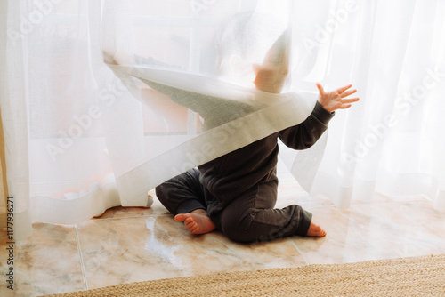 Toddler tangled in sheer curtain during playtime in a sunny room