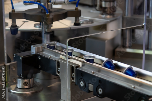 Close-up view of modern coffee pods making machine. Group of blue coffee capsules moves on narrow conveyer belt. Soft focus. Copy space. Coffee manufacturing plant theme.